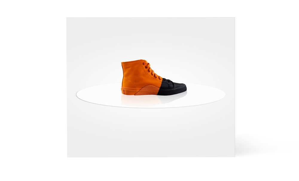 Orange shoe with black toe standing on glass plate.