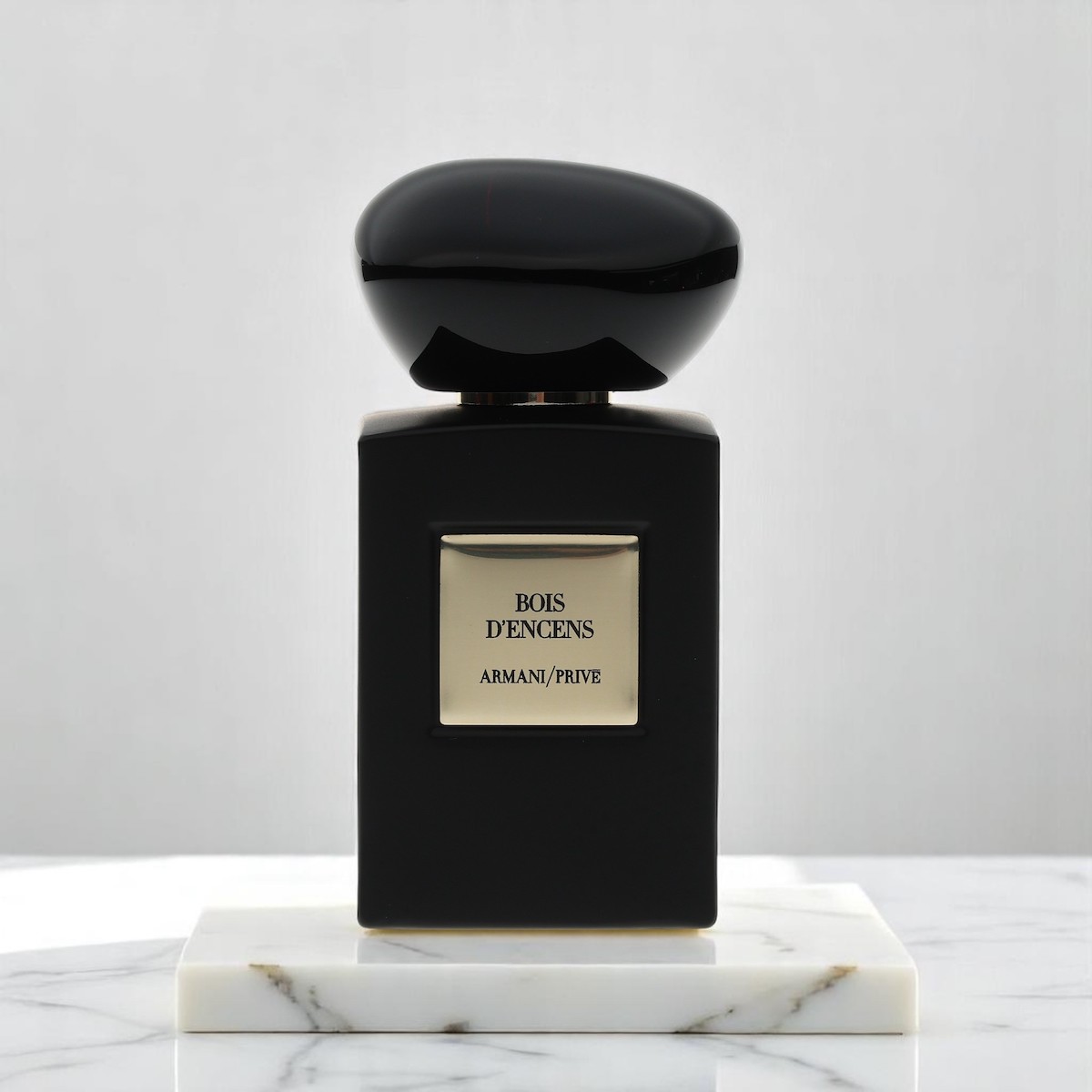 Bois D'Encens af Armani/Prive i en sort og guldflaske sidder oven på marmor på en matchende baggrund.